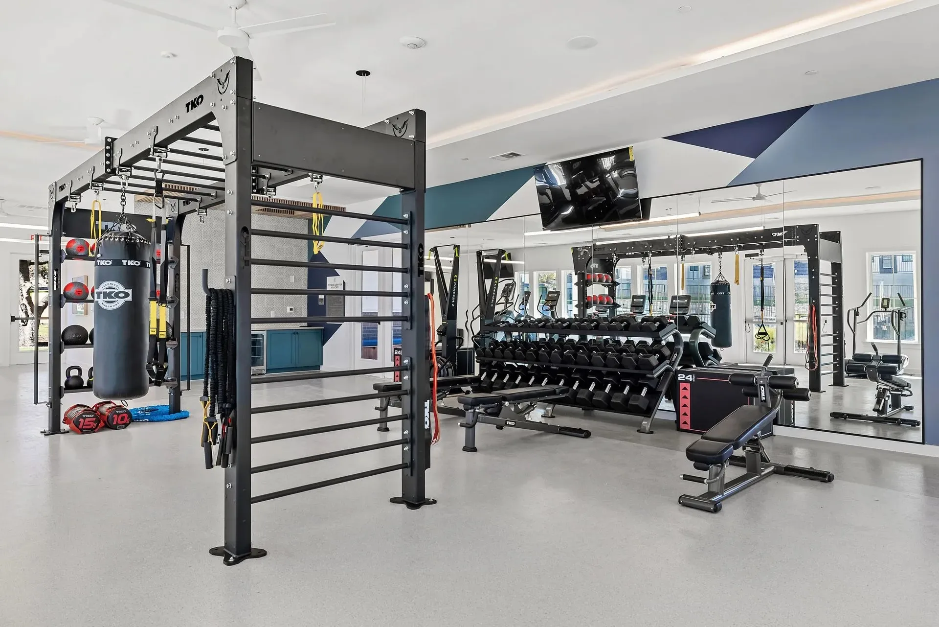 Apartment amenity gym in Austin, Texas, with a TKO functional rig, heavy bag, wall bars and a dumbbell rack