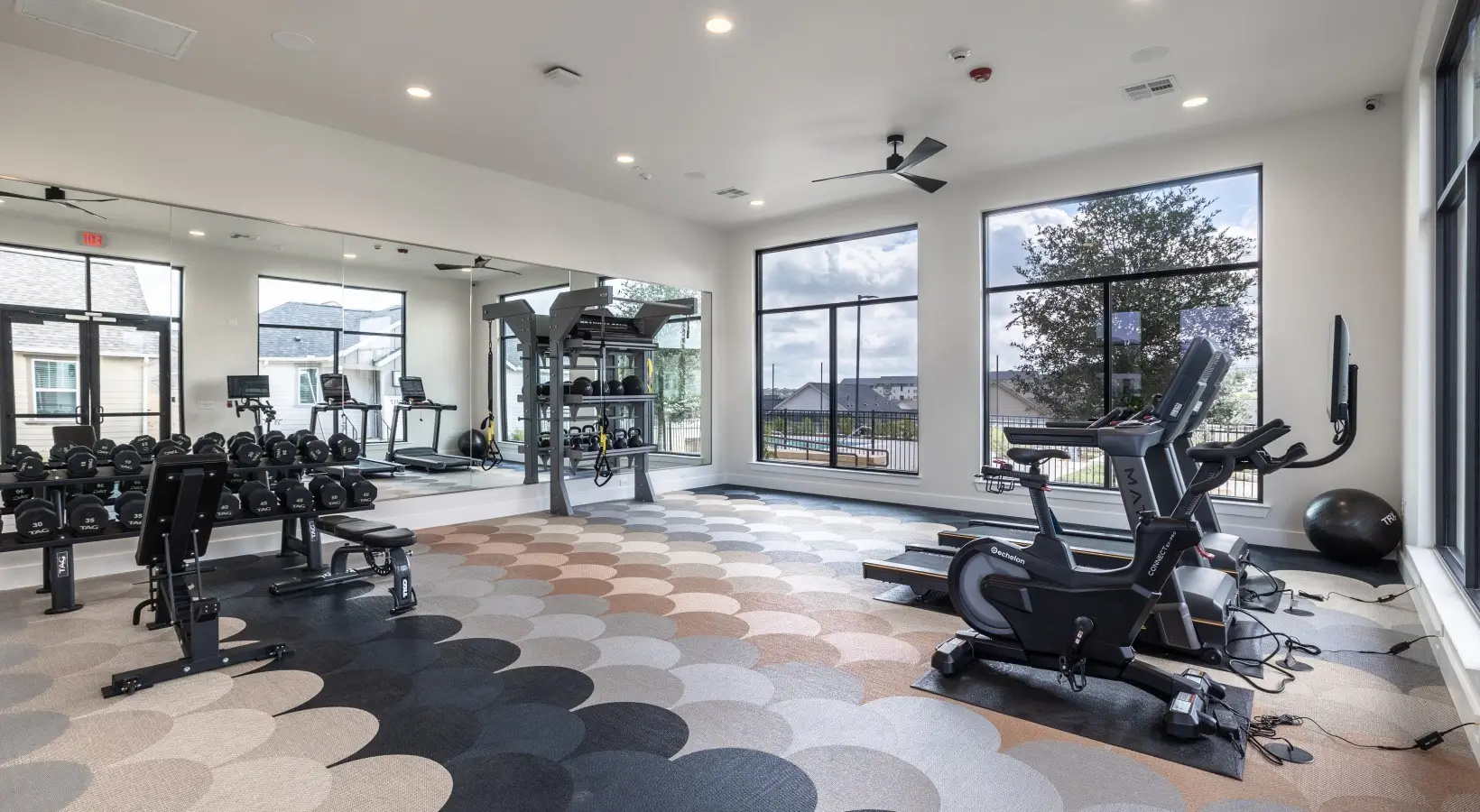 Apartment gym in Fort Worth, Texas, with TAG dumbbells and benches, a functional rig and an Echelon bike