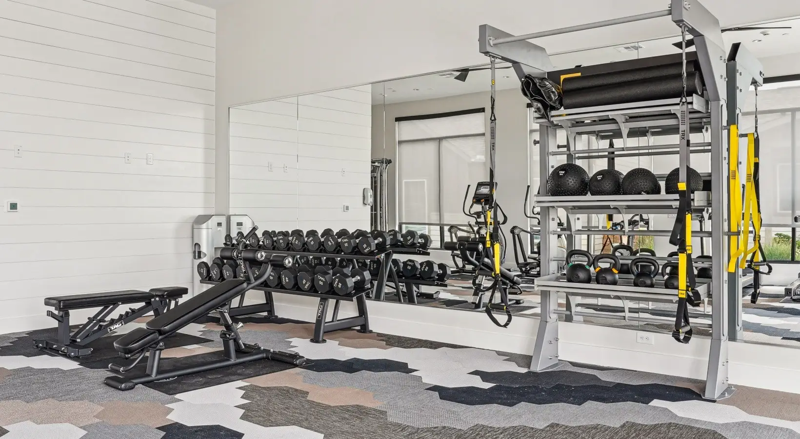 Free-weight area in a Fort Worth, Texas apartment gym with TAG dumbbells, benches and a TRX rack of kettlebells