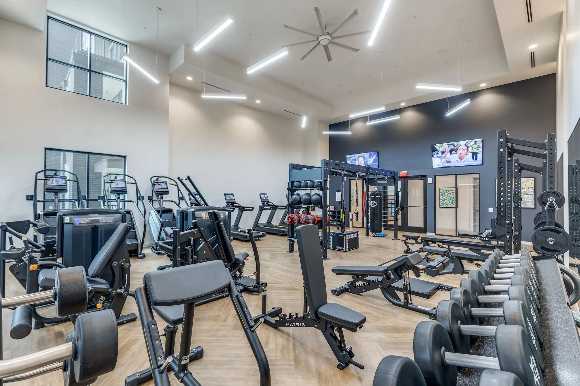 Apartment gym in Texas with Matrix leg machines, benches and dumbbells, a TKO rig and a stair climber