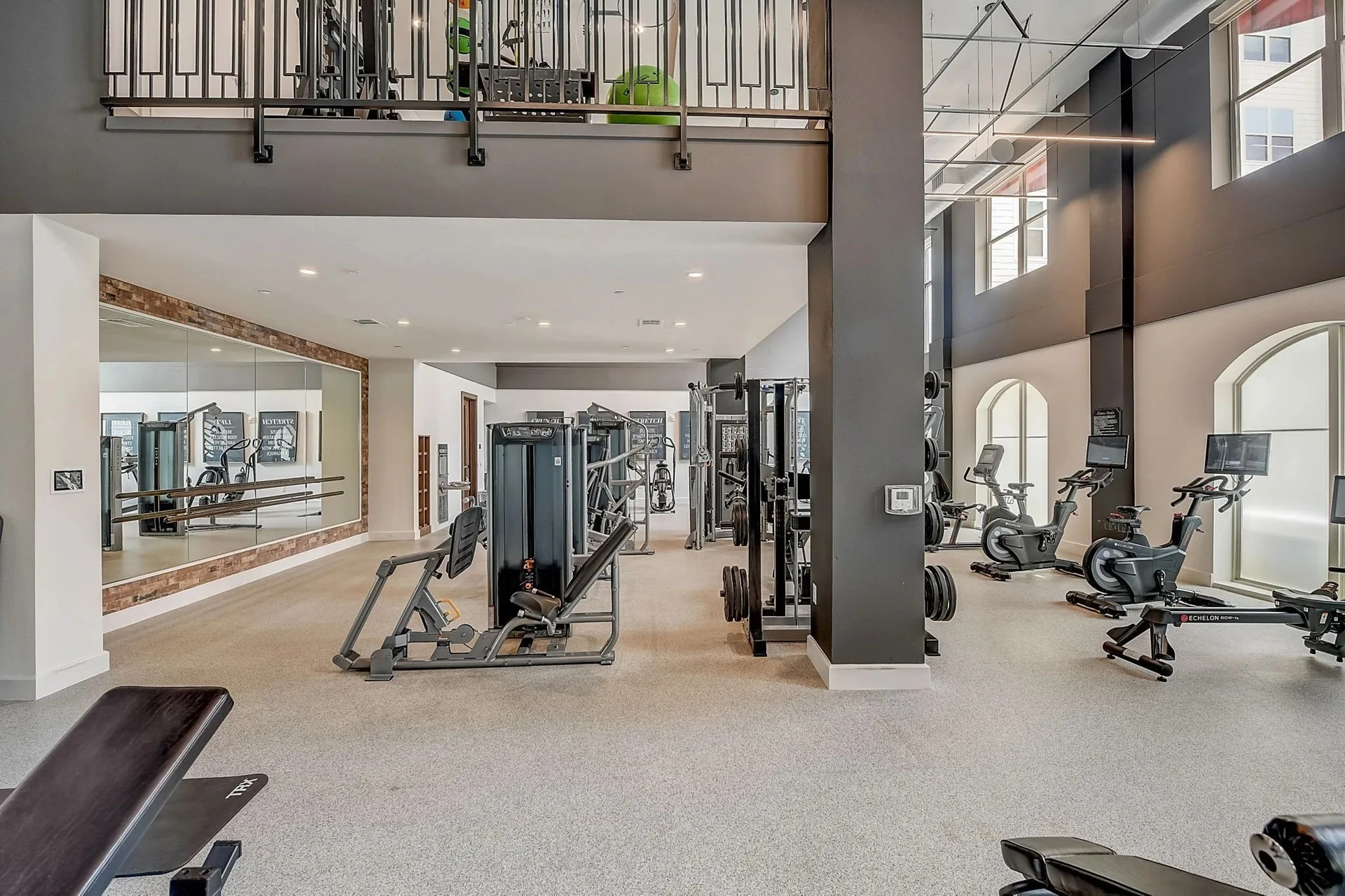 Double-height apartment amenity gym in Texas with a leg press, functional trainer, Echelon bikes and a rower