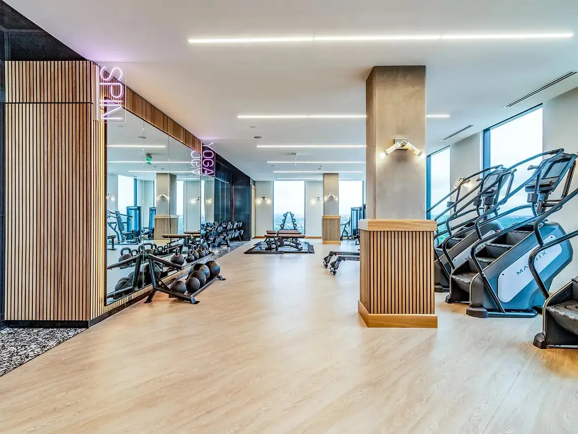 Fitness floor in Austin, Texas student housing with Matrix stair climbers, dumbbells and a spin studio beyond