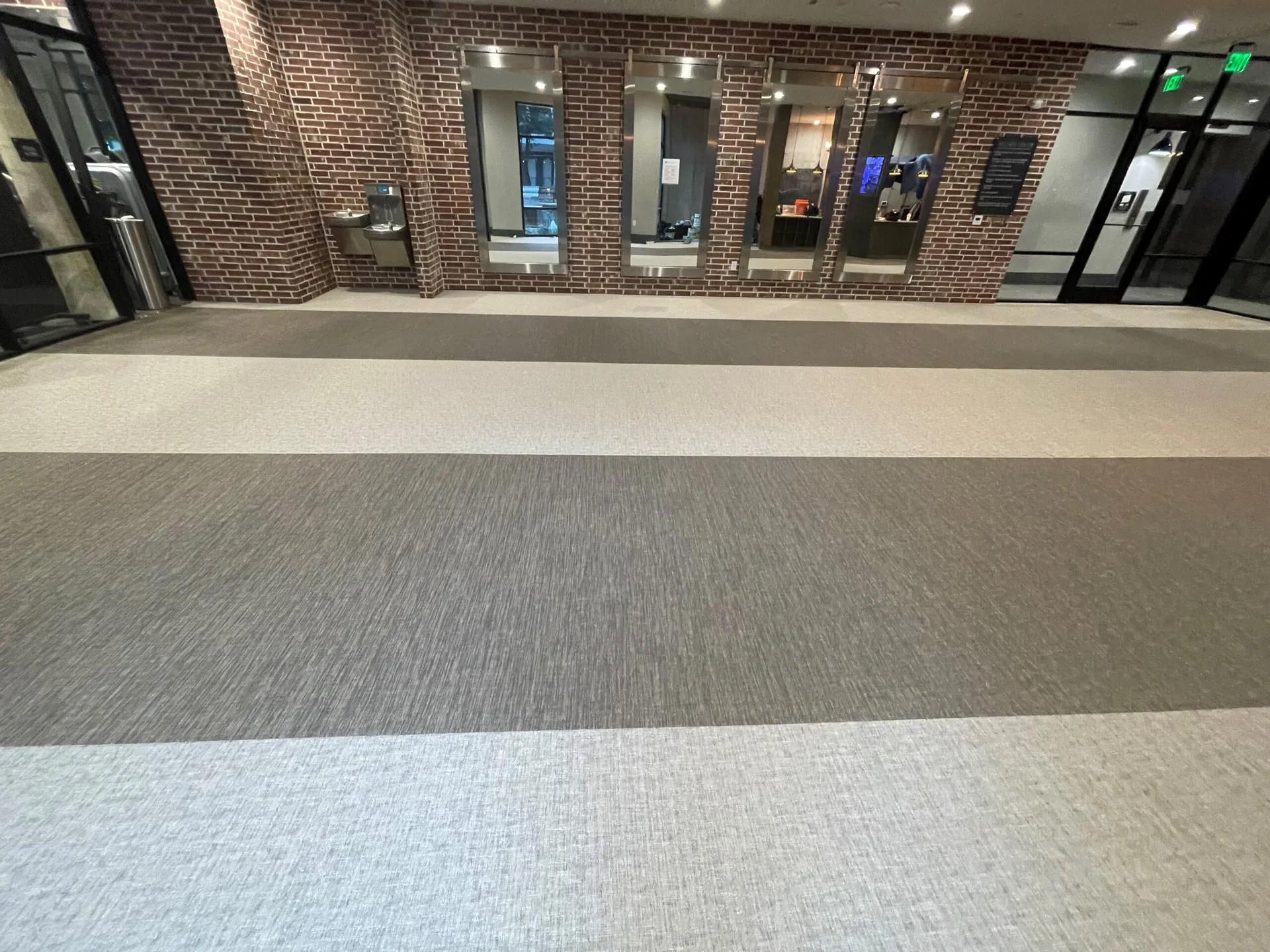 Woven vinyl flooring in wide grey and cream stripes through a fitness lobby with a brick wall and mirrors