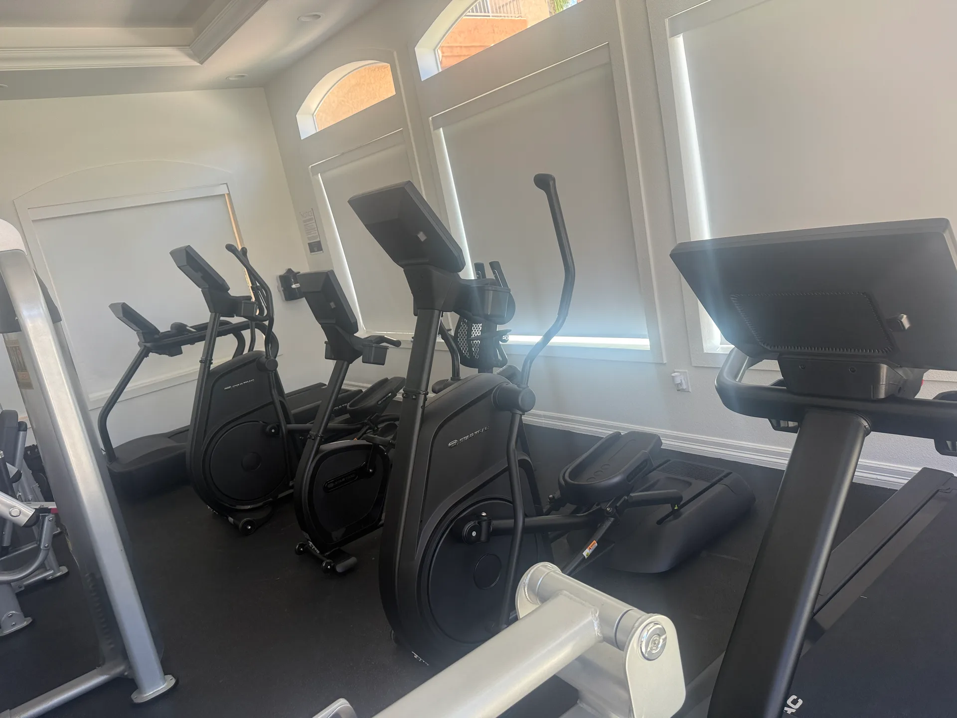 Ellipticals and a treadmill along a wall of arched windows at an Arizona apartment amenity gym