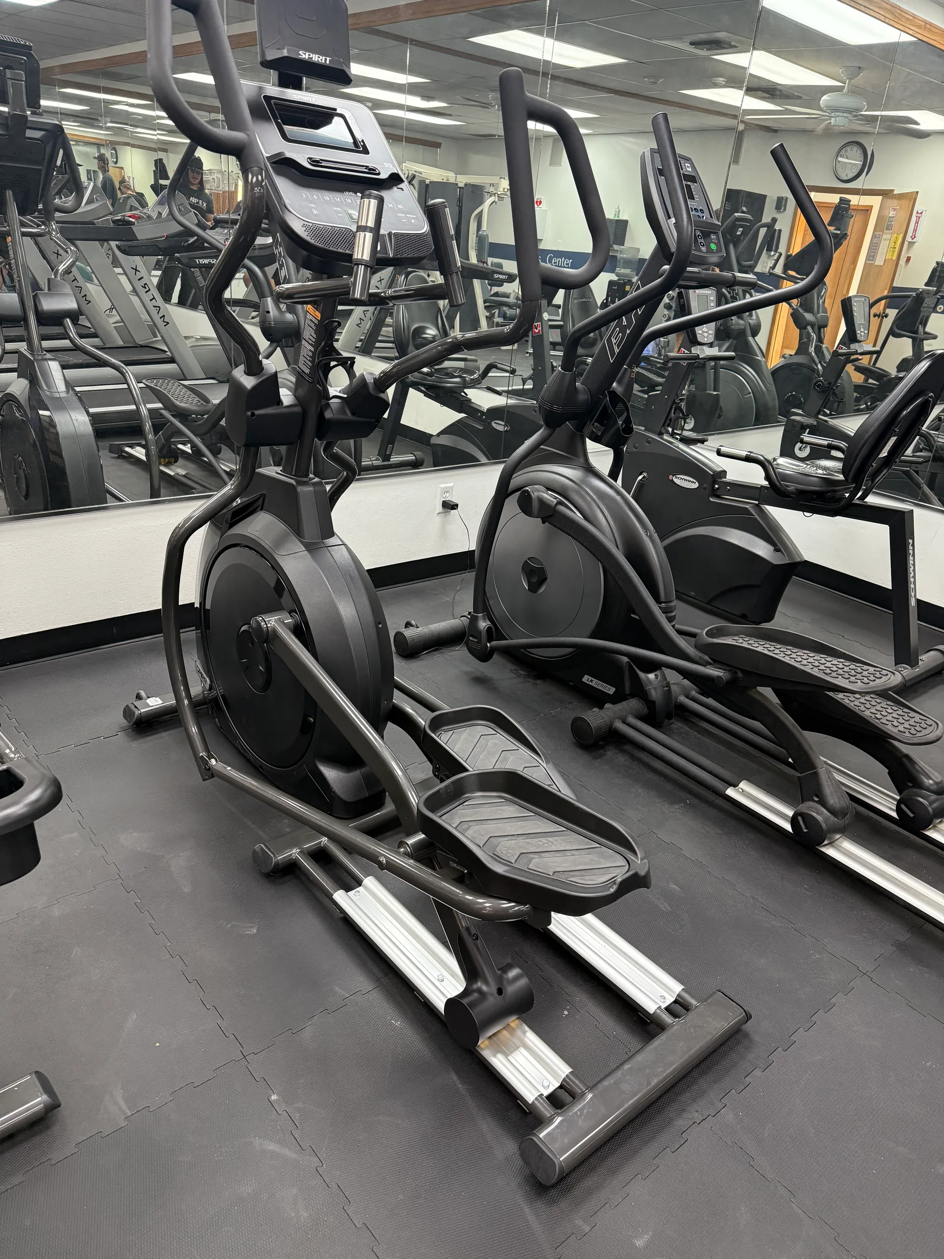 Two ellipticals at an Arizona apartment amenity gym, a Schwinn bike visible in the mirrored wall behind them