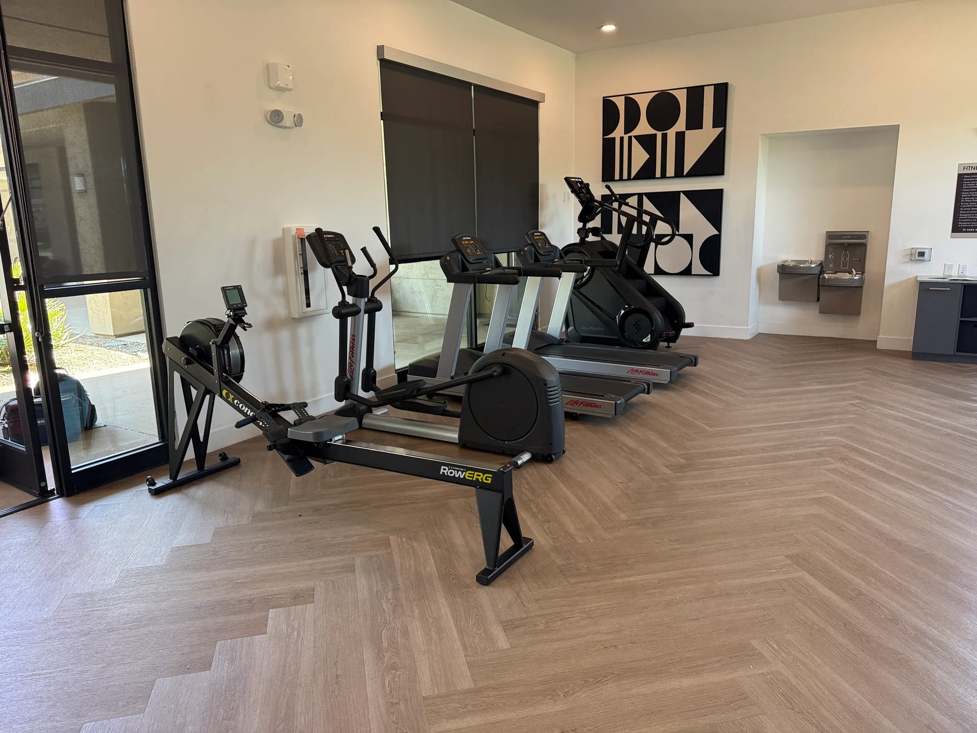 Concept2 RowErg and two Life Fitness treadmills on wood-look flooring at an Arizona apartment amenity gym