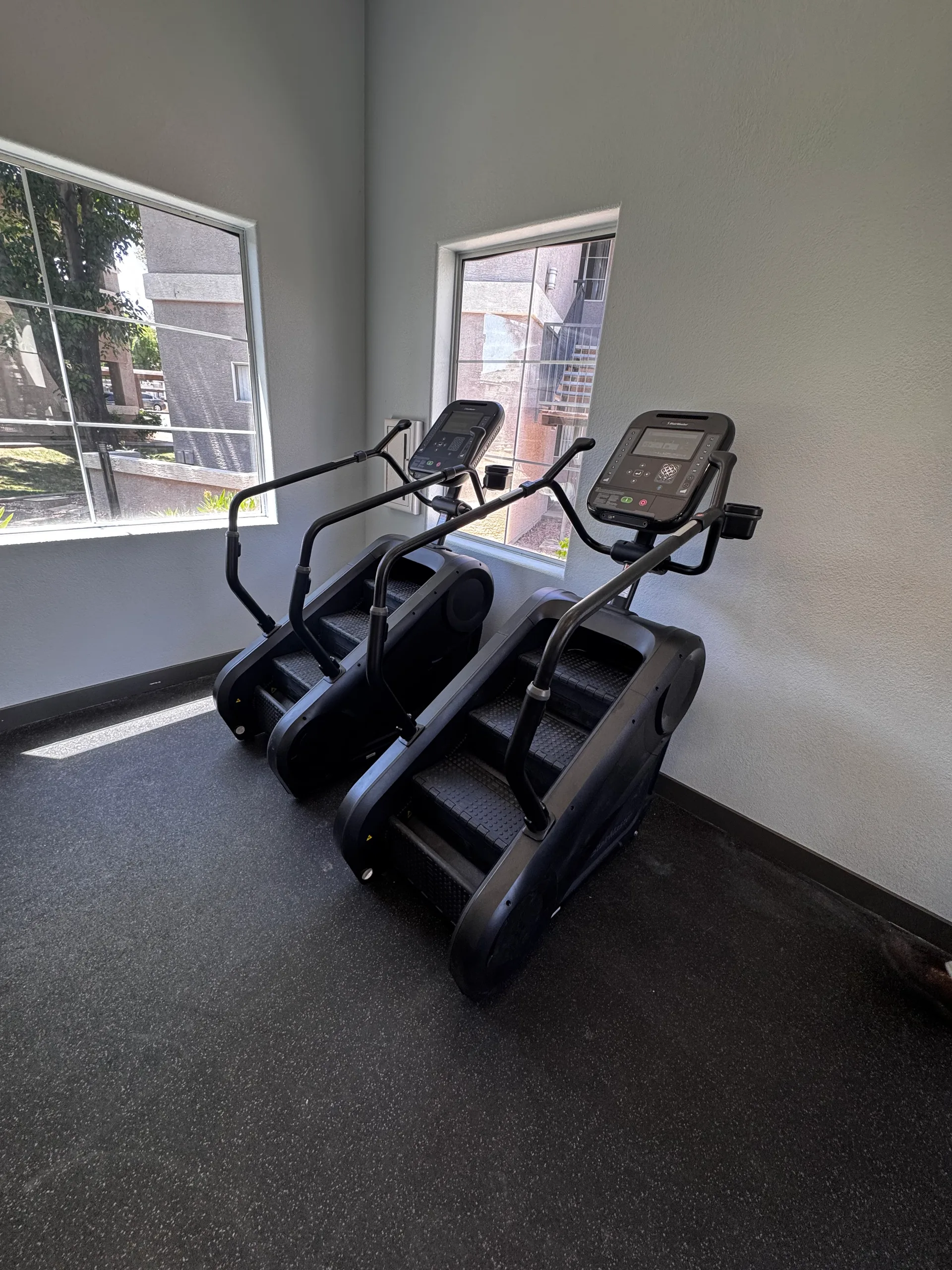 Two StairMaster-style step-mill climbers in a window corner at an Arizona apartment amenity gym