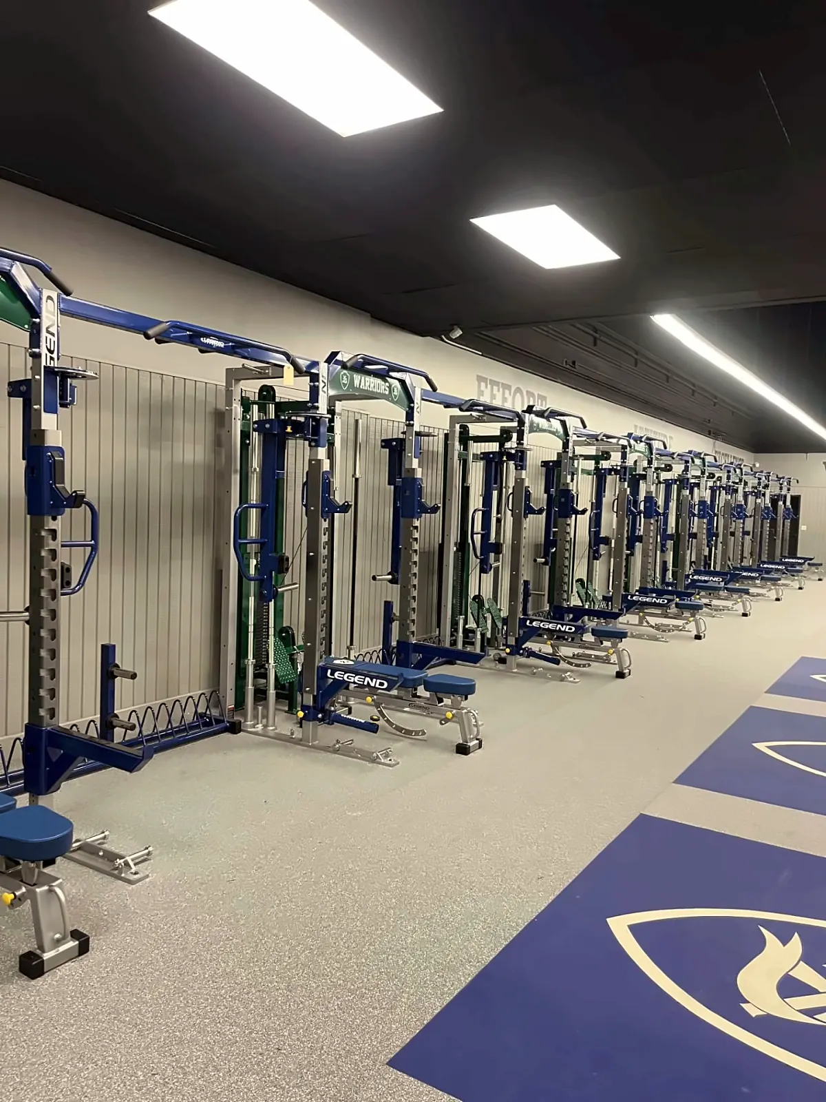 Little Rock Christian Academy weight room: navy shield-logo platforms in front of a long row of racks