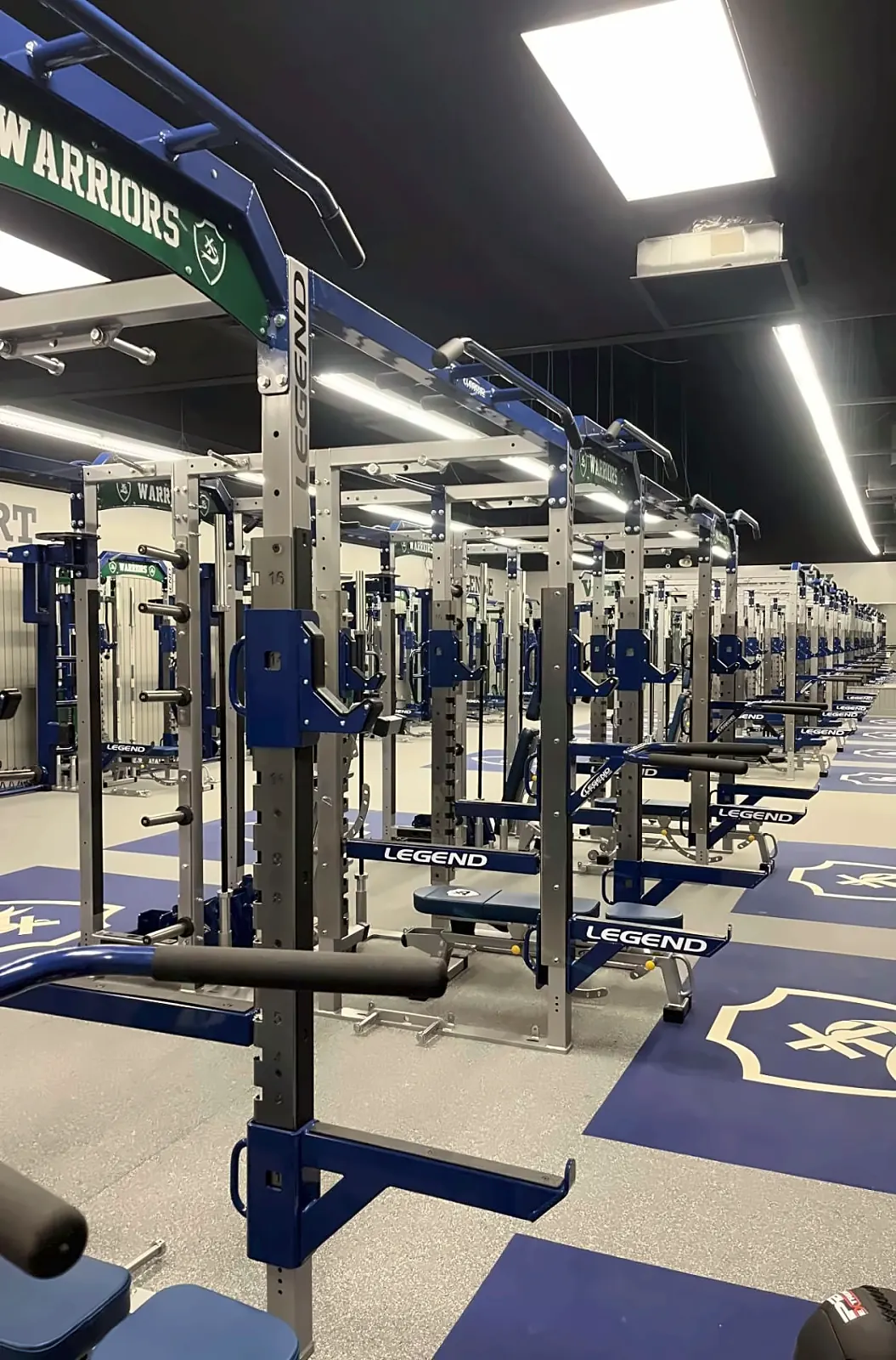 Little Rock Christian Academy weight room: a Warriors-branded rack row with adjustable benches and logo platforms