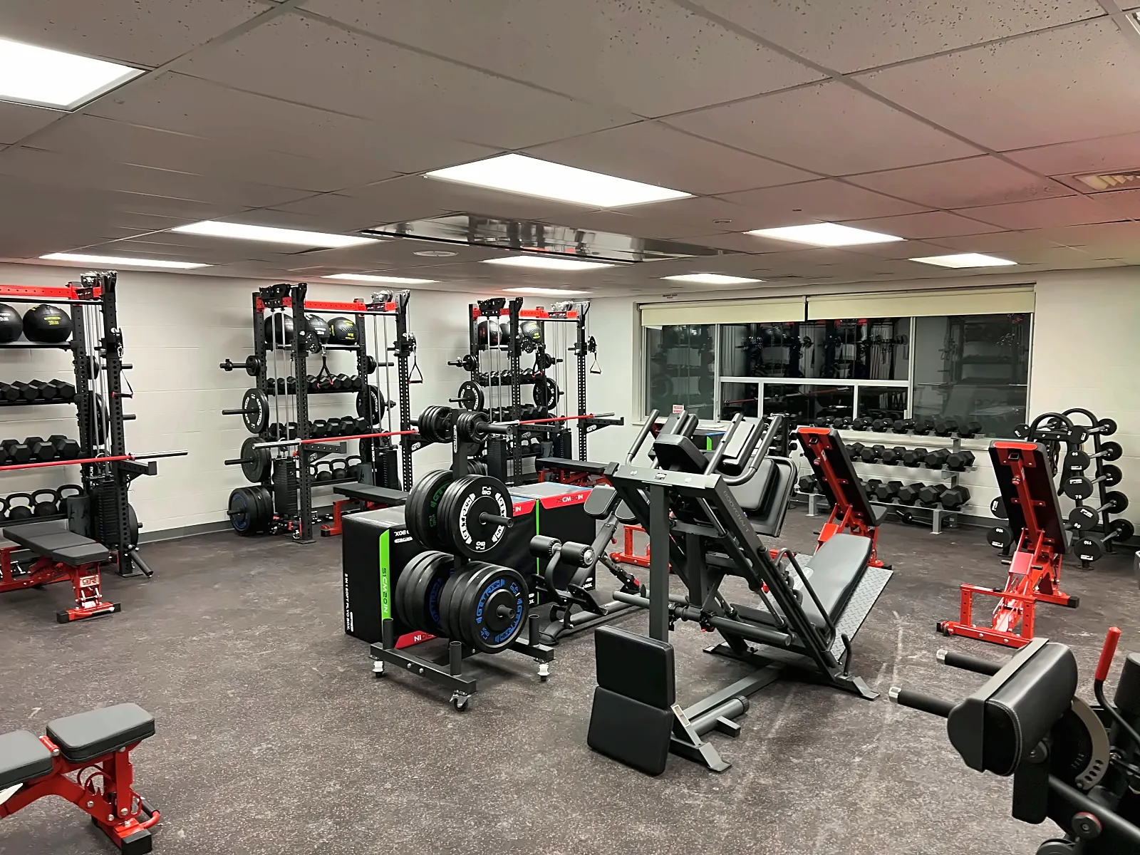 Saranac High School weight room: wall racks with ball and plate storage, a leg press and red benches