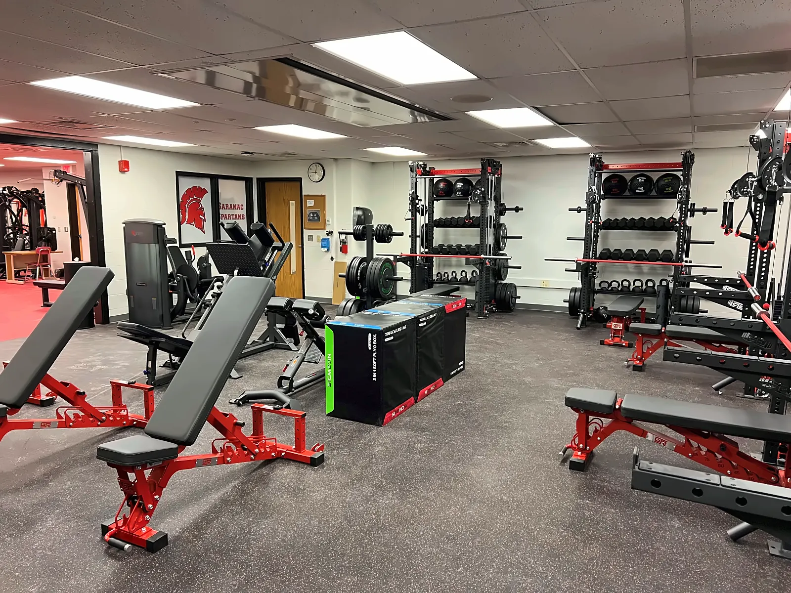 Saranac High School weight room: adjustable benches, plyo boxes and wall racks under the Spartans logo