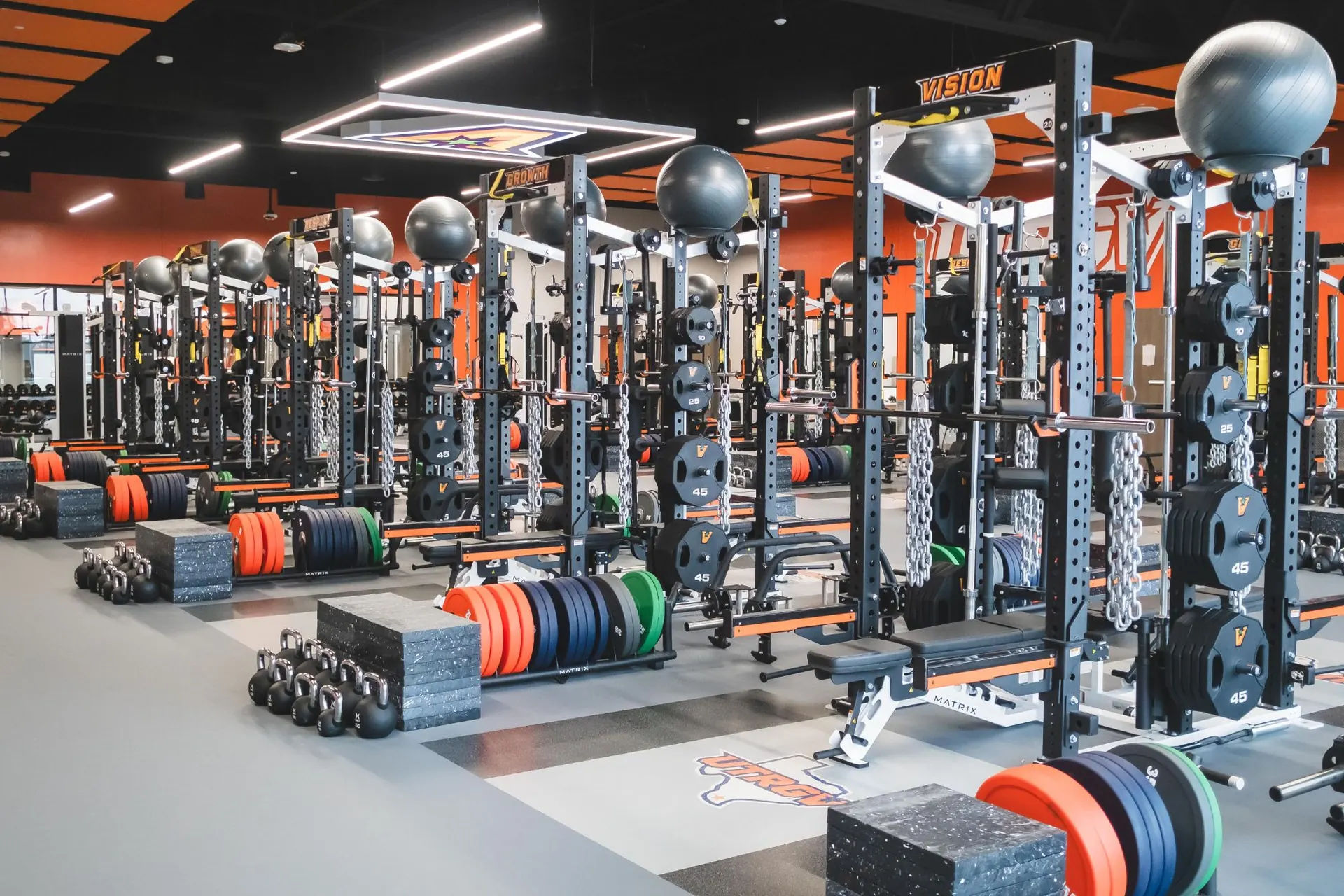 UTRGV weight room in Edinburg, TX: orange and black racks in rows with med balls, bumper plates and logo platforms