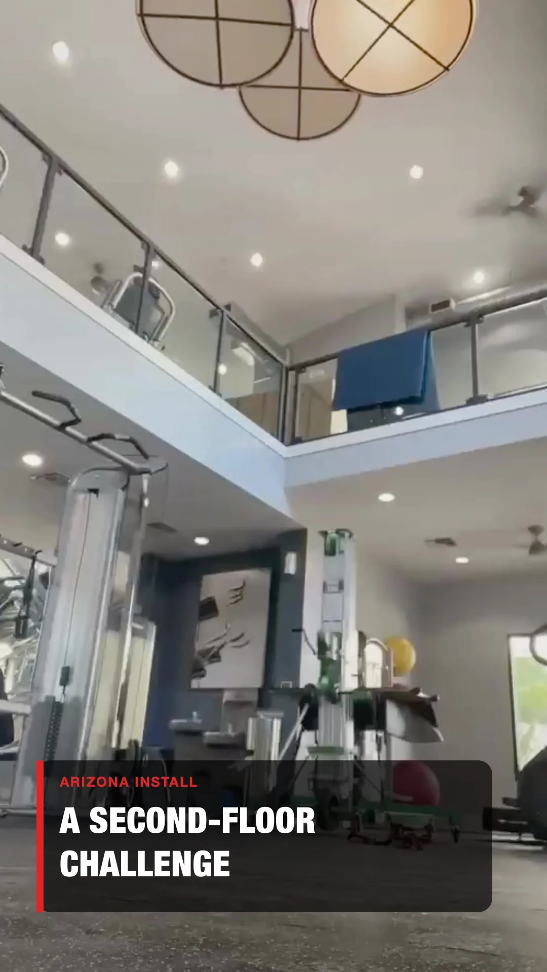A two-story amenity gym with an open, glass-railed mezzanine and a powered material lift positioned on the ground floor
