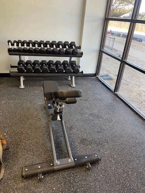 Ab bench and dumbbell rack by a window wall in a Bedford, Texas parks and recreation fitness room