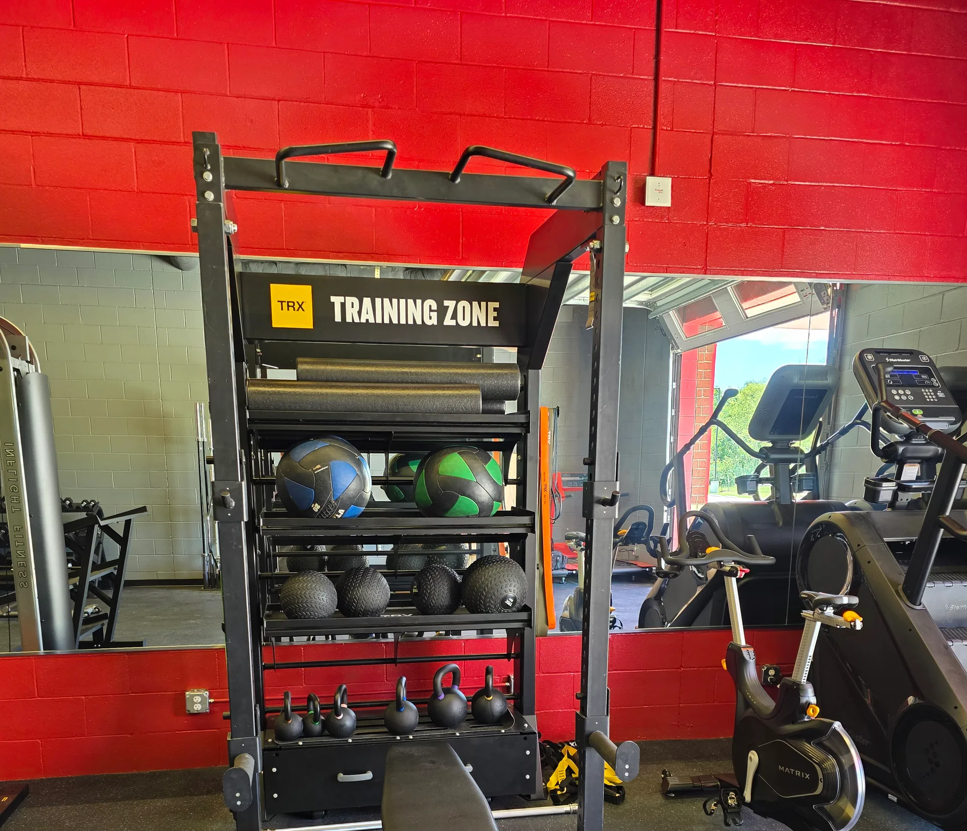 TRX suspension training zone with wall shelving, a mirror and a stair climber in a Buda, Texas fire station gym