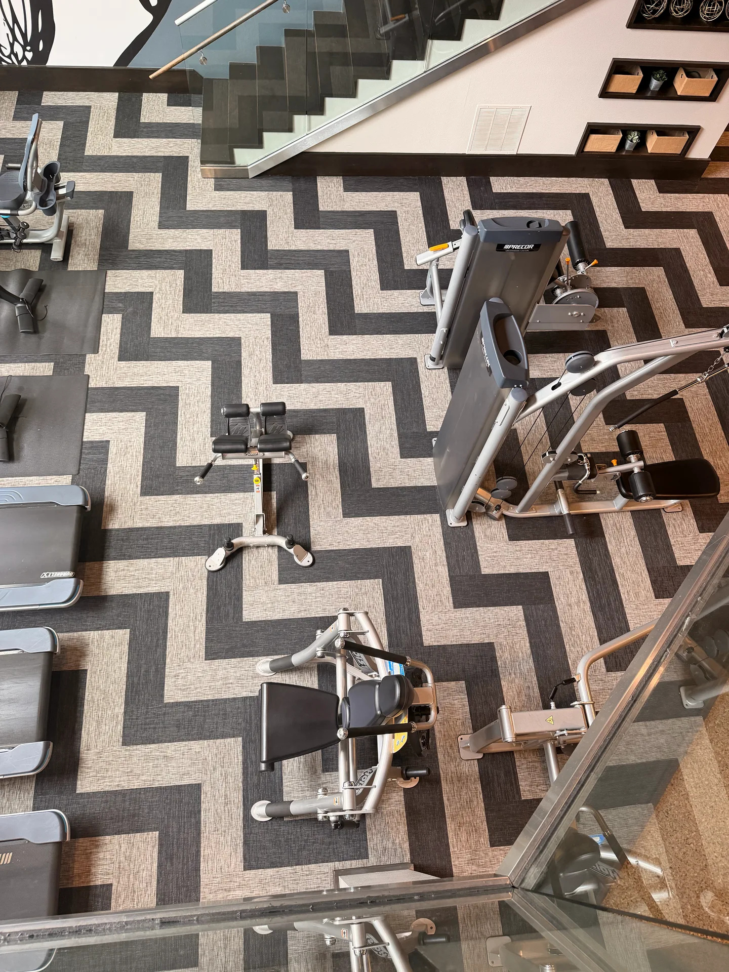 Overhead view of two-tone chevron plank flooring and strength machines in a two-story Dallas, Texas apartment gym