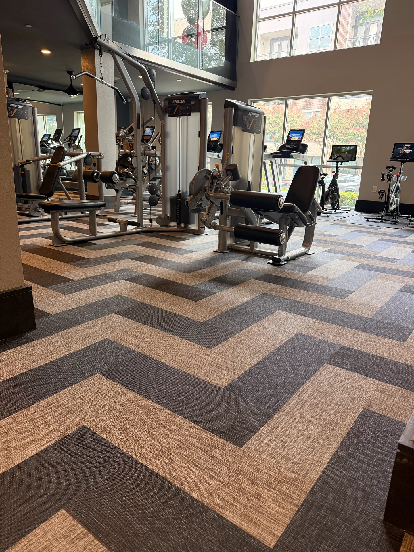 Chevron plank flooring in charcoal and parchment under a selectorized strength line in a Dallas, Texas apartment gym