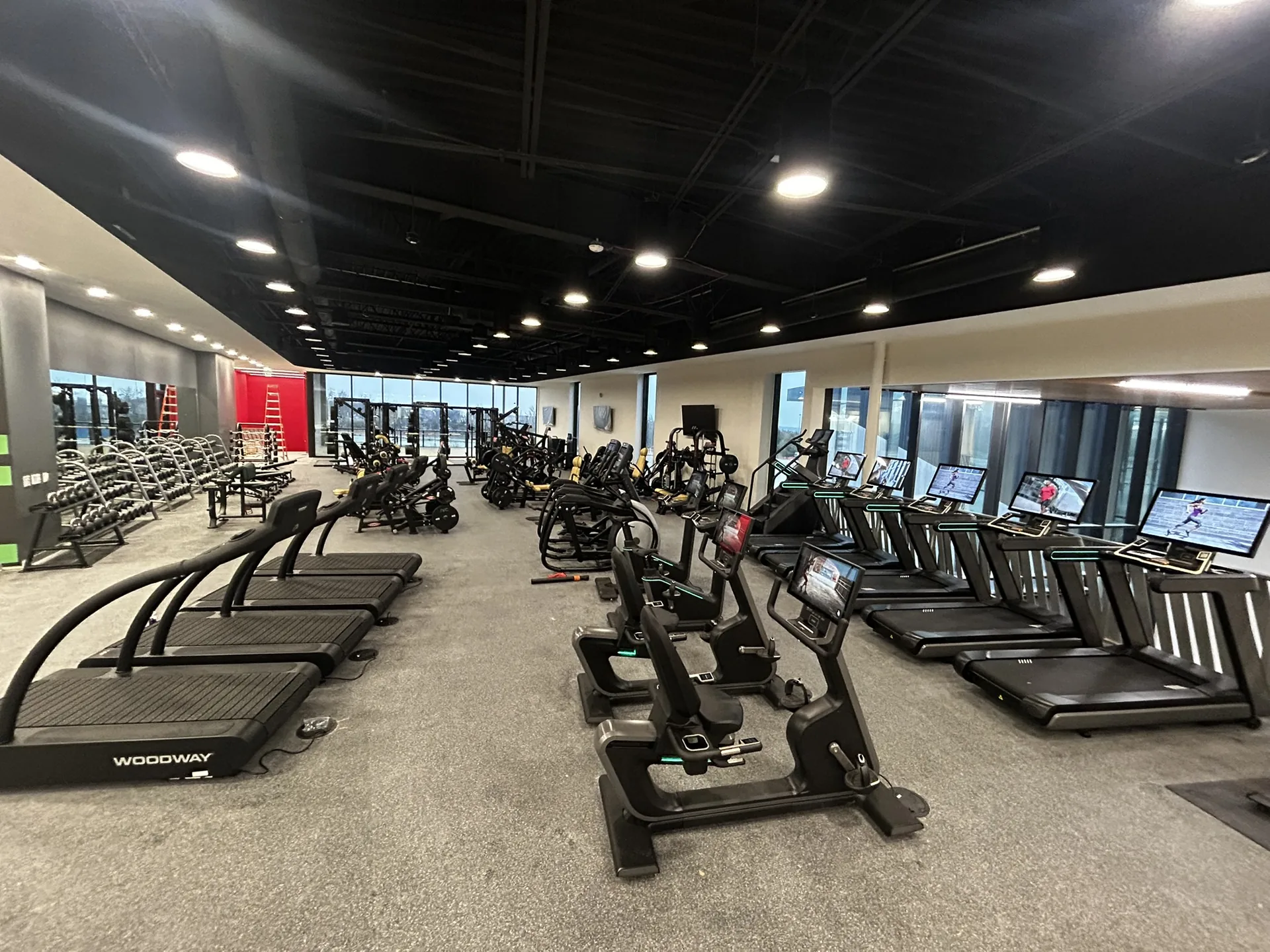 A recreation center cardio floor with four Woodway slat-belt treadmills, Matrix bikes and treadmills, and dumbbell racks
