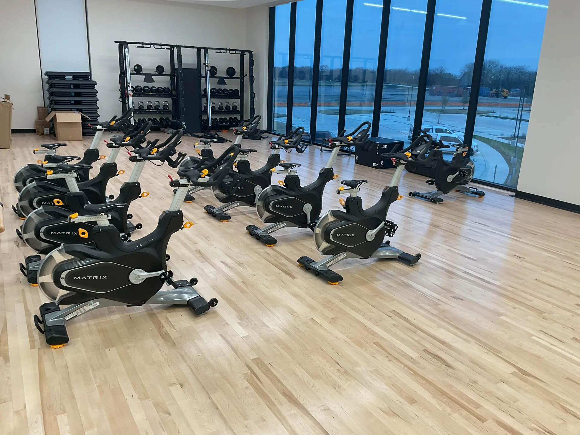 An indoor cycling studio with Matrix group cycles on a maple hardwood floor beside a floor-to-ceiling window wall