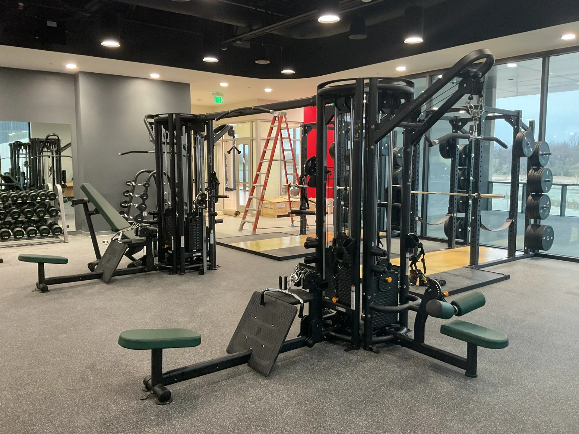 A multi-station functional training rig with cable stations and benches, dumbbell racks and a mirrored wall behind it