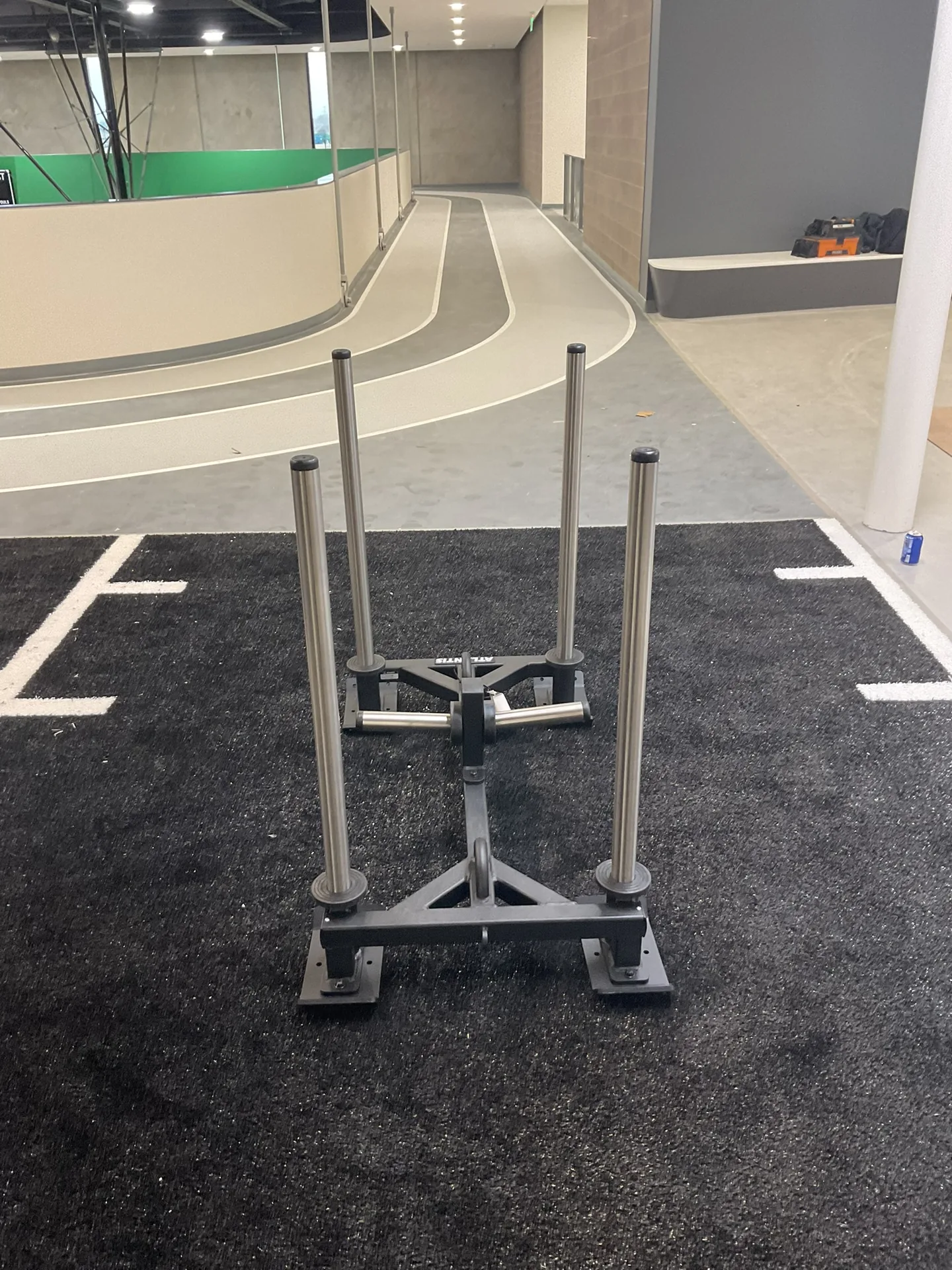 A weighted push sled on a black turf lane beside a banked indoor walking and running track