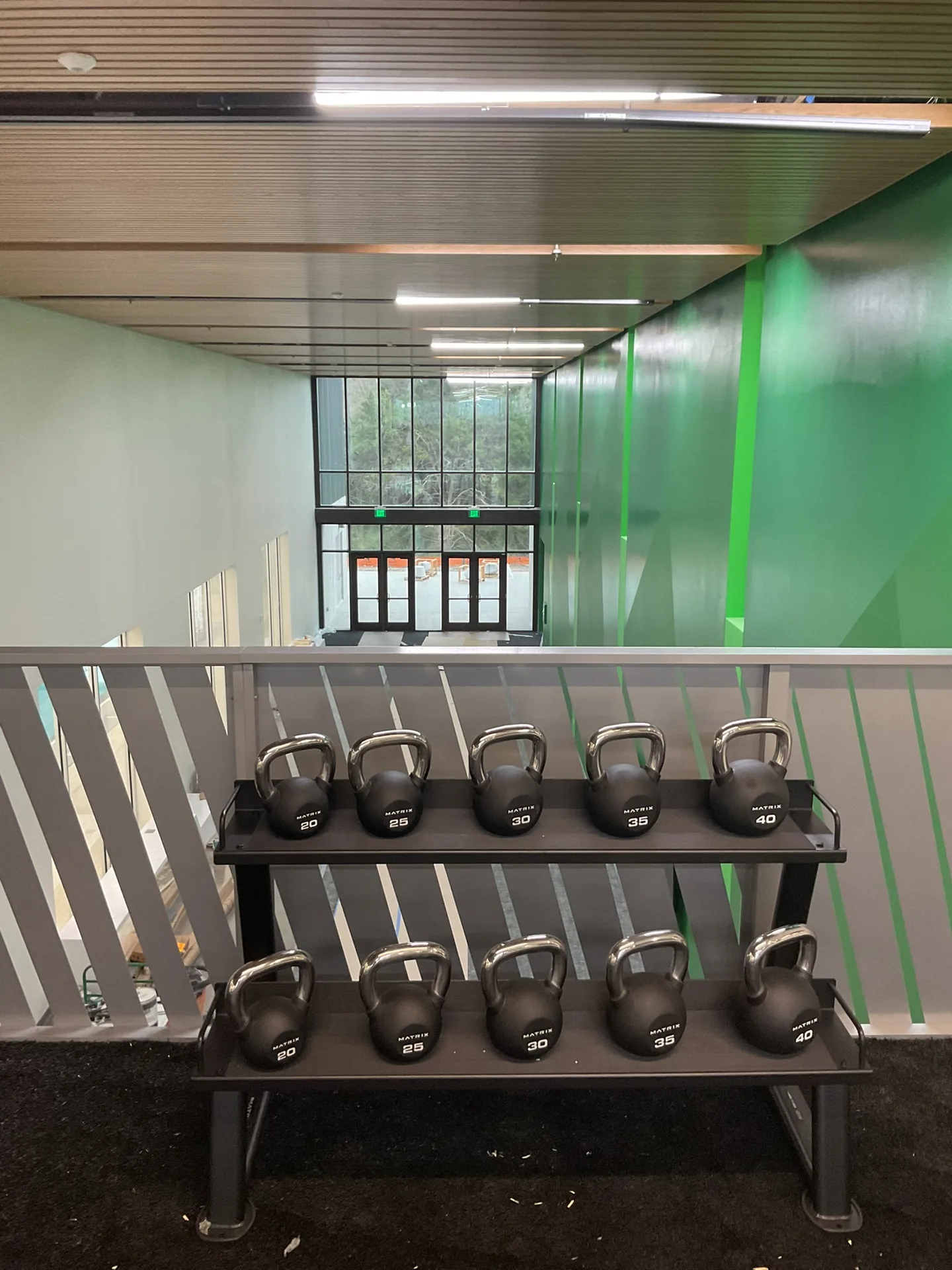 A two-tier kettlebell rack on turf beside a glass wall overlooking the pool concourse