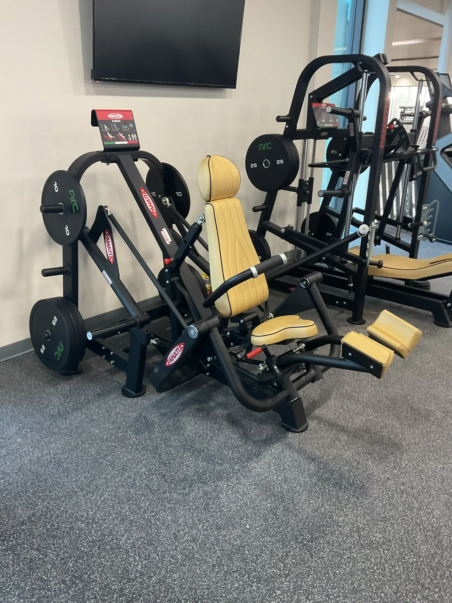 A Panatta plate-loaded leg press and converging machines with tan upholstery, loaded with bumper plates