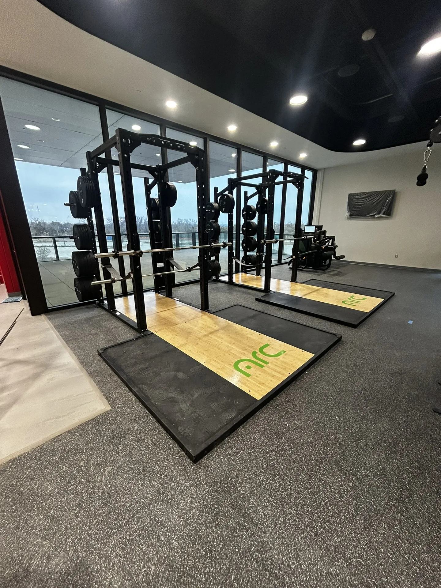 Two Matrix Magnum power racks loaded with bumper plates, on custom wood lifting platforms by a window wall