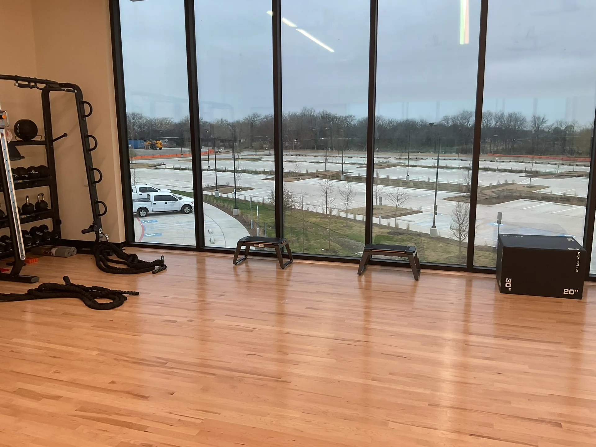 A maple-floored studio room with a functional rig, plyo box and floor-to-ceiling windows