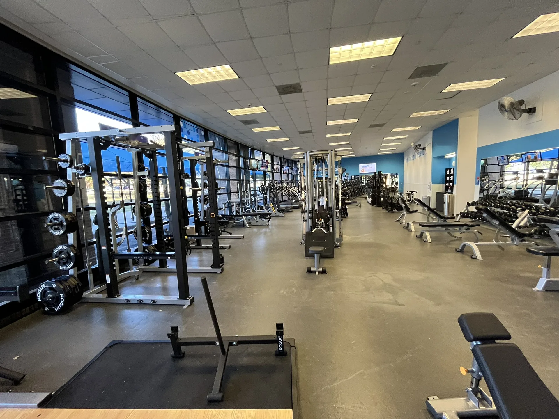Long view of a Fort Worth corporate fitness center: racks by the windows, a cable column, benches and dumbbells