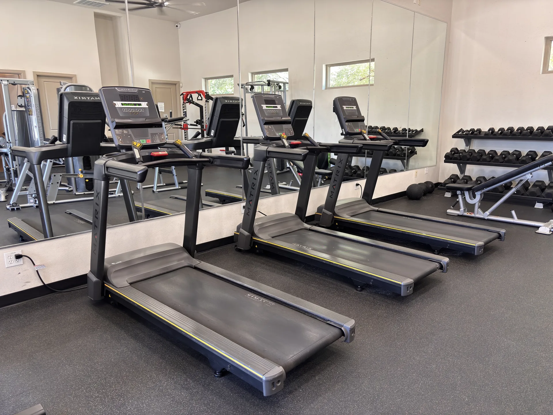 Row of Matrix treadmills along a mirror wall with a dumbbell rack behind in a Grand Prairie, Texas HOA fitness center