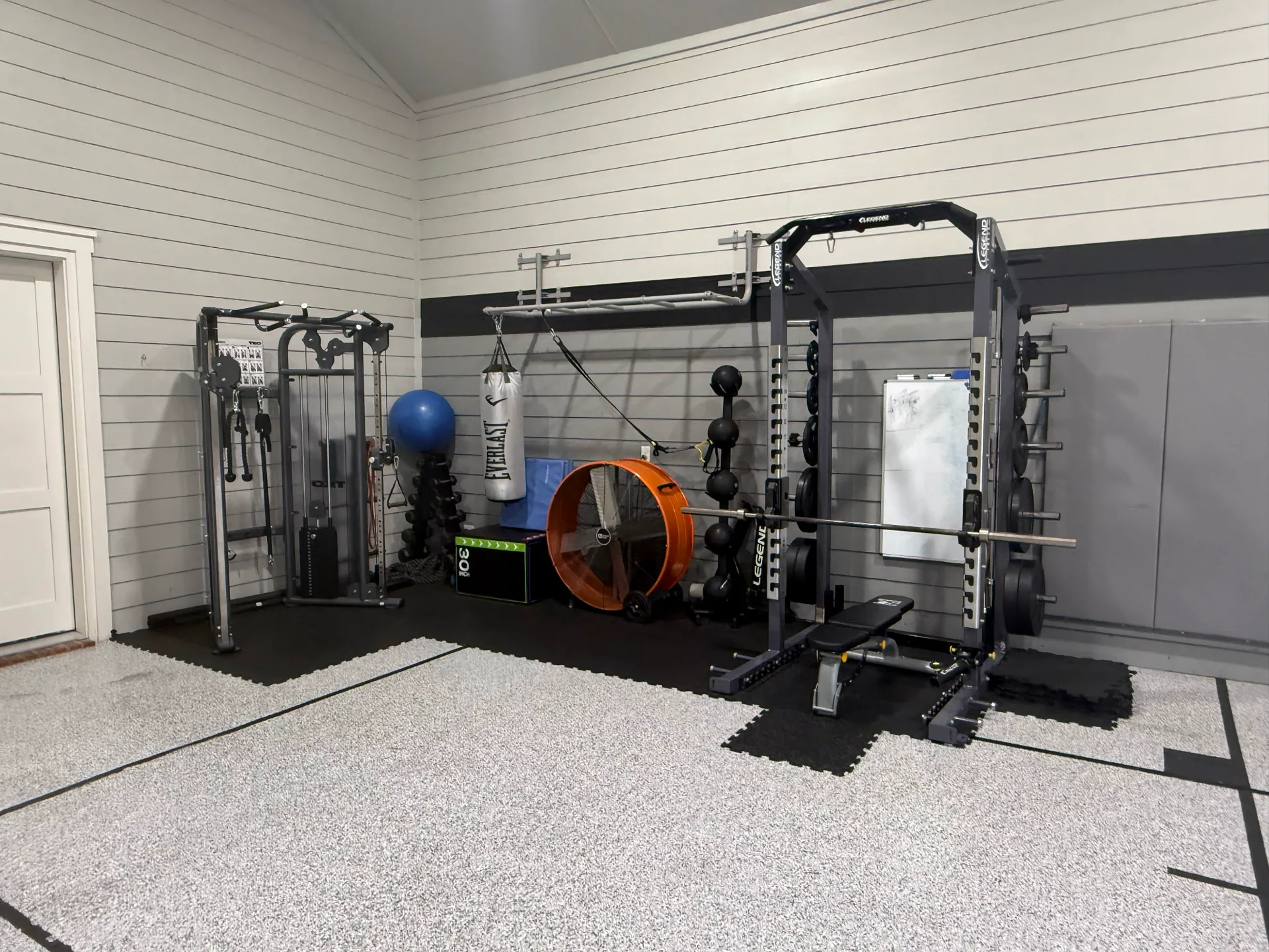 Garage home gym in Plano, Texas: a functional trainer, a rack and a heavy bag on rubber tiles by shiplap walls