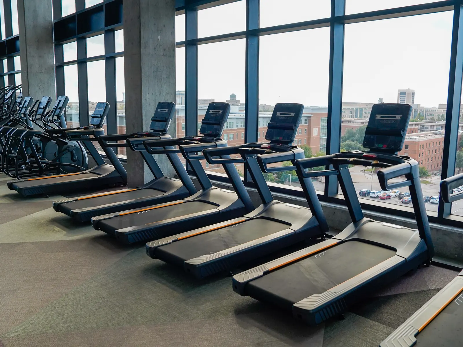 Row of treadmills facing floor-to-ceiling windows in a Texas student housing fitness center