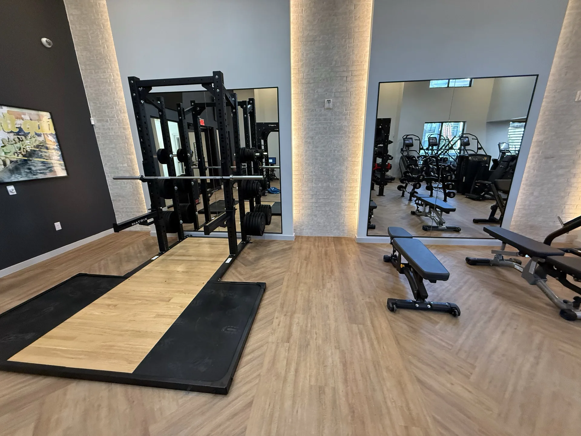 Matrix half rack on a lifting platform with a hardwood insert beside backlit brick pilasters in a Houston apartment gym