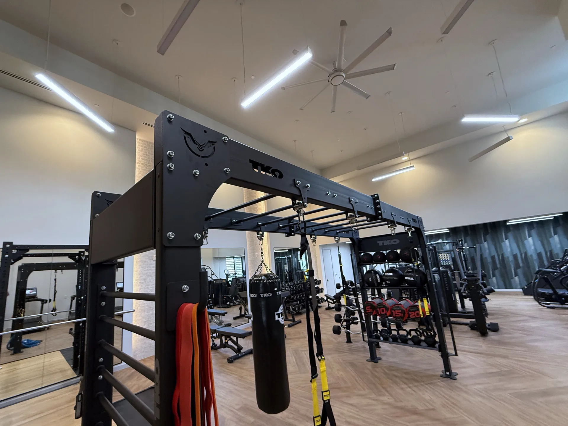 TKO 14-foot bridge rig with a heavy bag, TRX straps and ball storage on herringbone floor in a Houston apartment gym