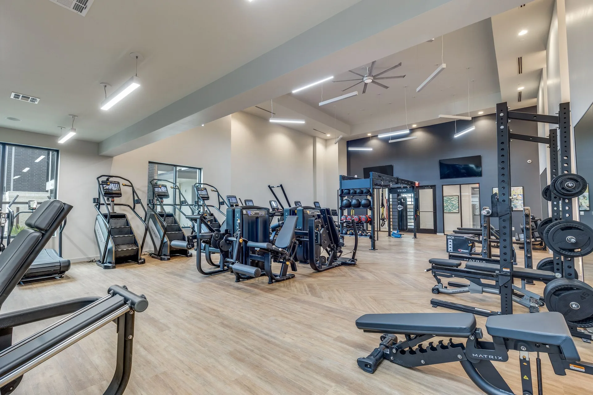 Matrix climbmills, a strength line and a half rack with plates across a Houston apartment fitness center