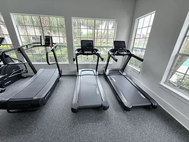 Curved manual runner and two Spirit treadmills facing palm-tree windows in a Houston, Texas apartment gym