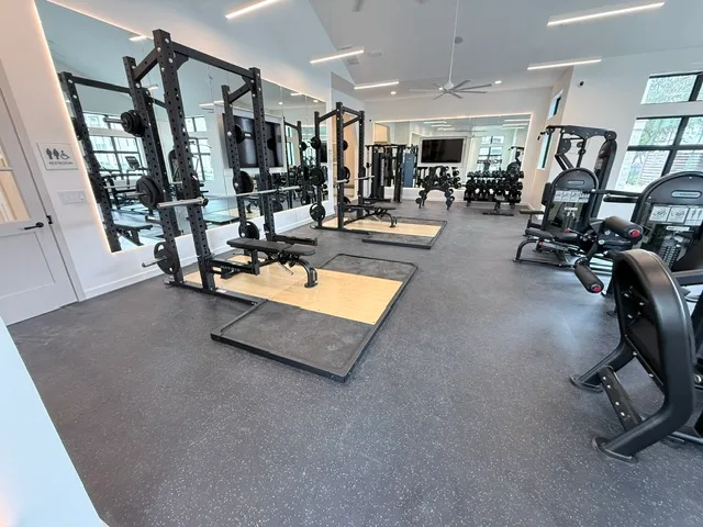 Two Matrix half racks on hardwood-inlay platforms with a mirror wall and dumbbell rack in a Katy, Texas apartment gym