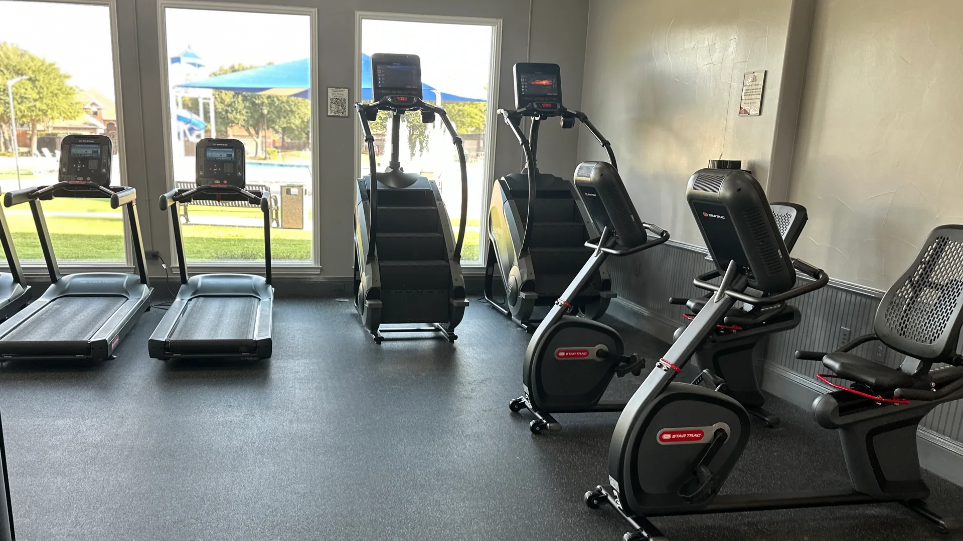 Star Trac treadmills, two stair climbers and recumbent bikes at windows onto a pool at a Lavon, Texas HOA fitness center