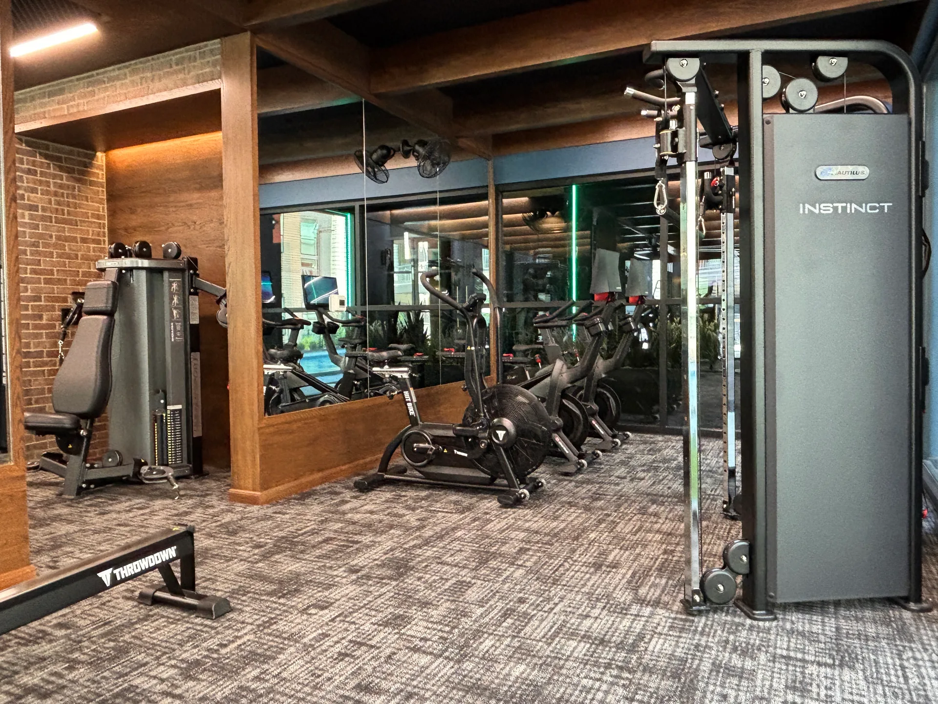 Instinct cable column, air bike and connected bikes in a wood-paneled corner of a Mansfield, Texas apartment gym