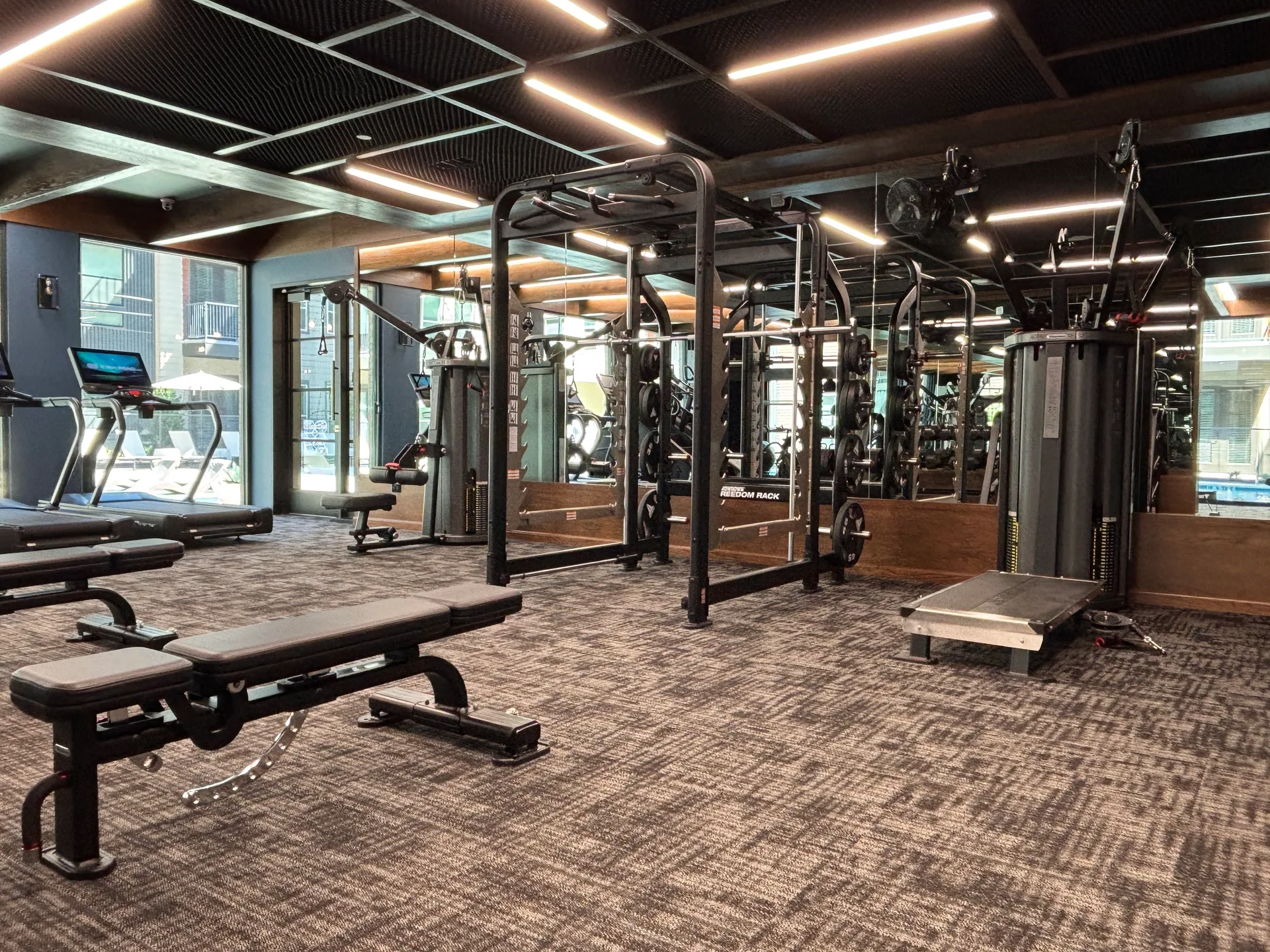 Freedom rack, benches and cable station along a mirror wall under timber beams in a Mansfield, Texas apartment gym