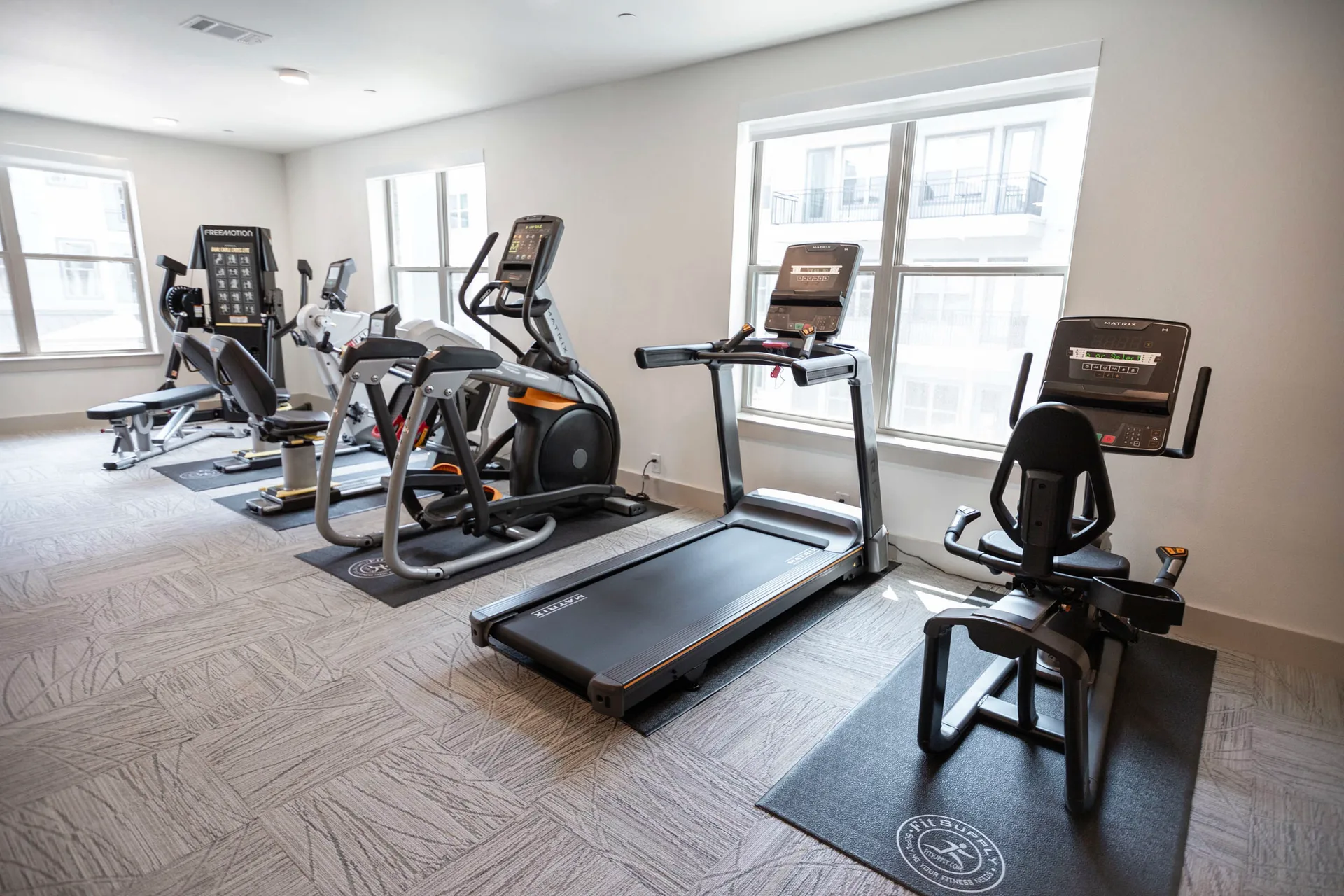 Matrix treadmill, recumbent bike and Ascent Trainer with SciFit steppers along windows in a McKinney senior living gym