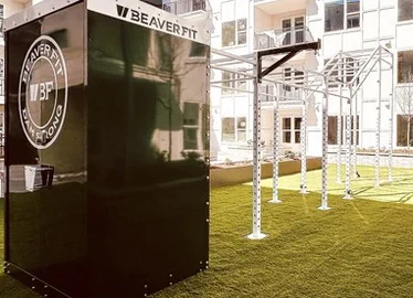 Weatherproof lockable storage container beside an outdoor training rig on turf