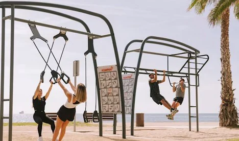 People training on an outdoor functional rig with suspension trainers and climbing holds near the coast