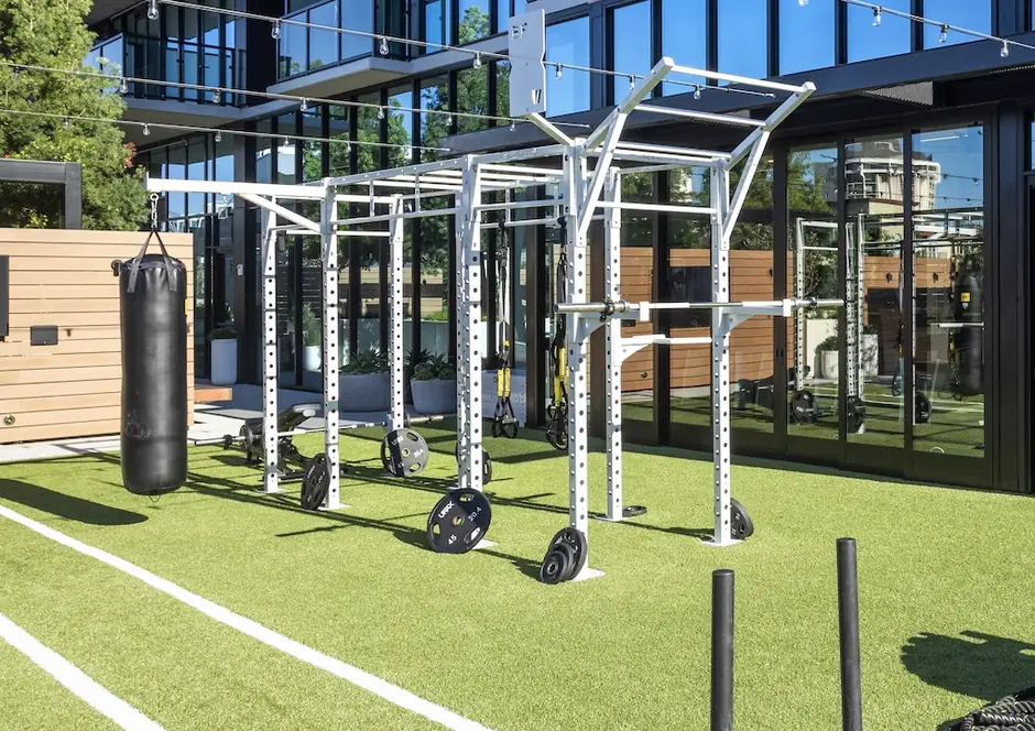 Outdoor rig bolted to base plates through turf at an apartment community, with a heavy bag and bumper plates