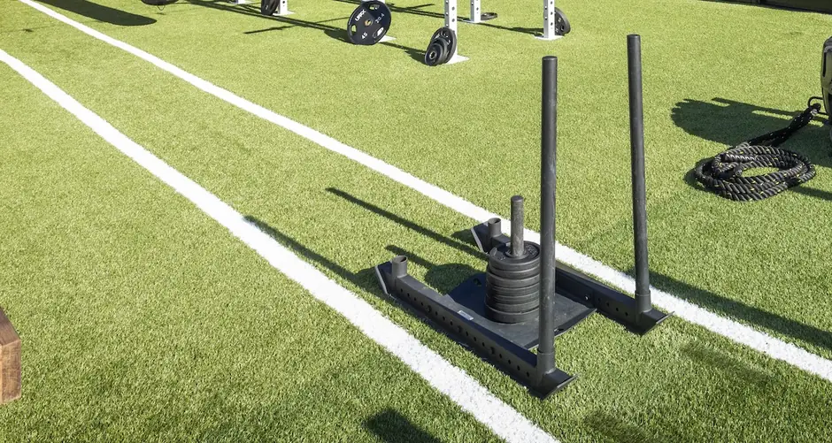 Artificial turf with painted sprint lanes, a loaded sled and battle ropes in an outdoor training zone