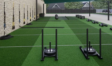 Outdoor turf training lane with weighted sleds and wall-mounted suspension trainers