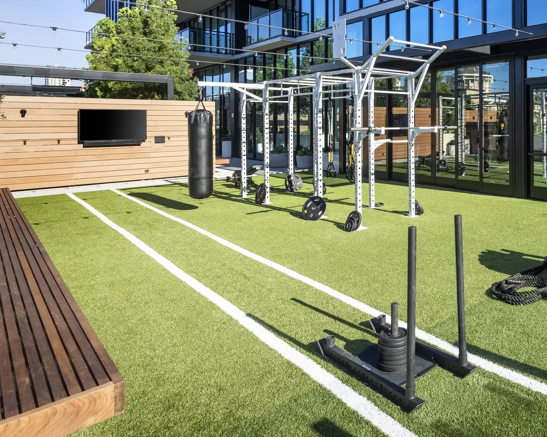Outdoor turf zone with sprint lanes, a weighted sled, battle ropes and a rig with a heavy bag