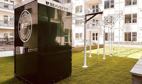 Weatherproof lockable storage container beside an outdoor training rig on turf at an apartment community