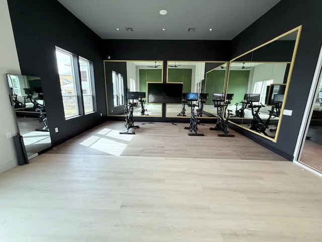 Cycling studio with Star Trac virtual bikes facing a screen and gold-framed mirrors in a Spring, Texas apartment gym